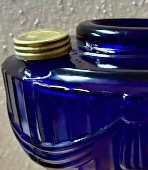 Close-up of a deep blue glass container with a small gold-colored screw cap on its side.