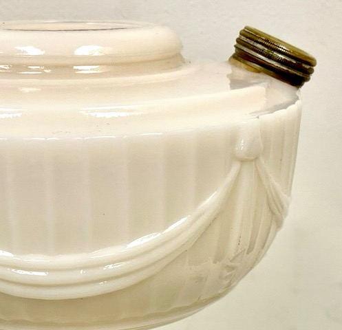 Close-up of a vintage white ceramic jar with raised decorative garlands and a metal screw-on cap leaning on its side.