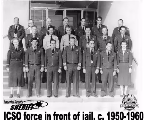 Black and white photo of 18 Imperial County Sheriff officers posing in uniform in front of a jail, circa 1950-1960.