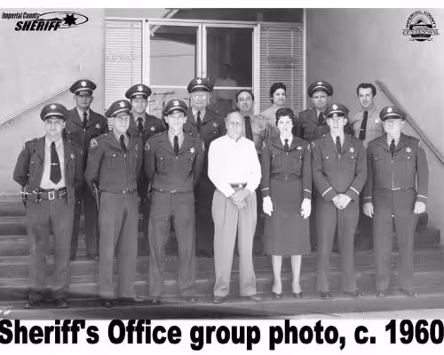 Black and white group photo of Imperial County Sheriff's Office staff circa 1960, with fourteen officers and one civilian posed in front of building steps.