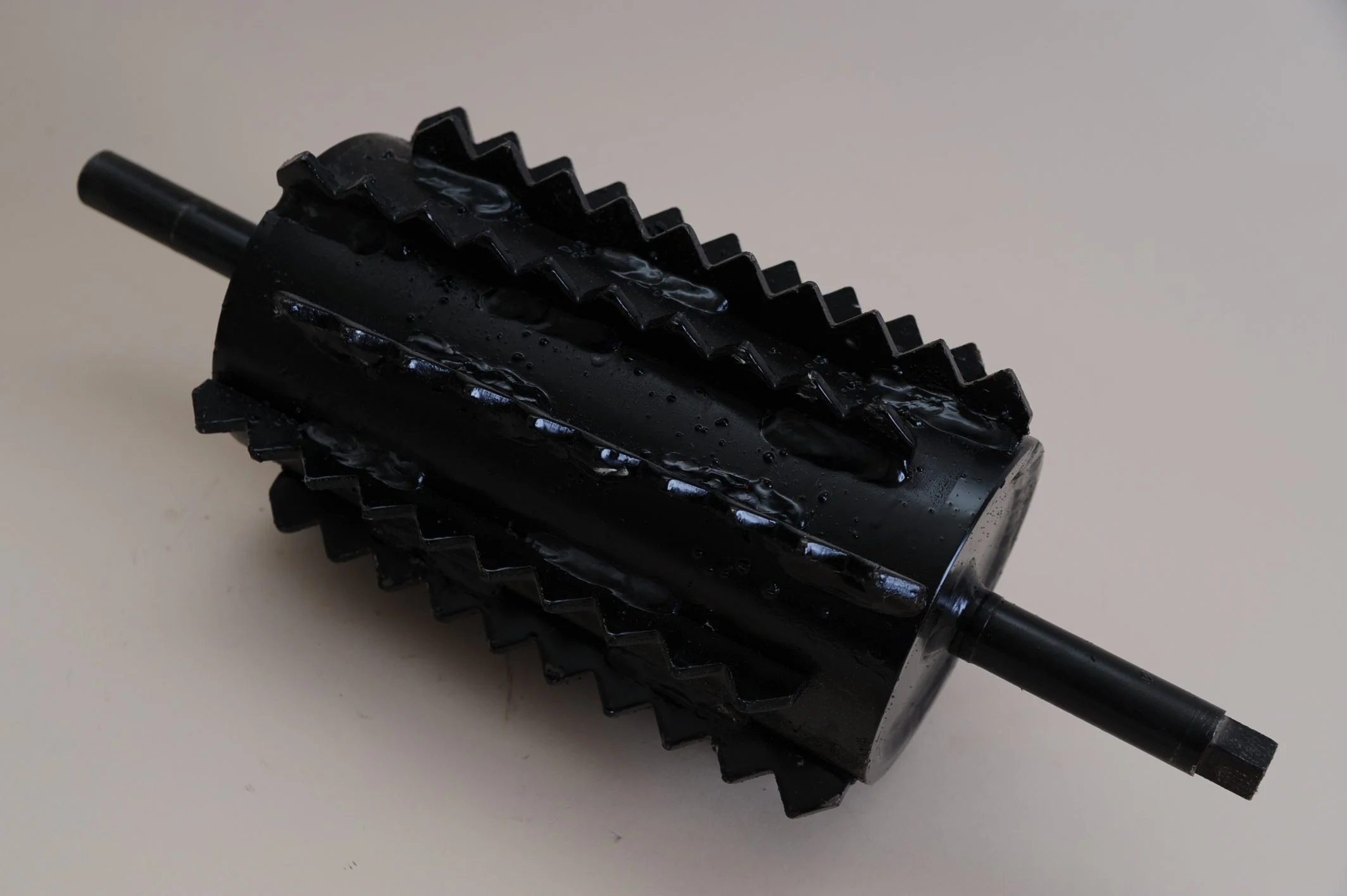 Black metal feed roller with zigzag teeth on its cylindrical surface and shaft ends on both sides.