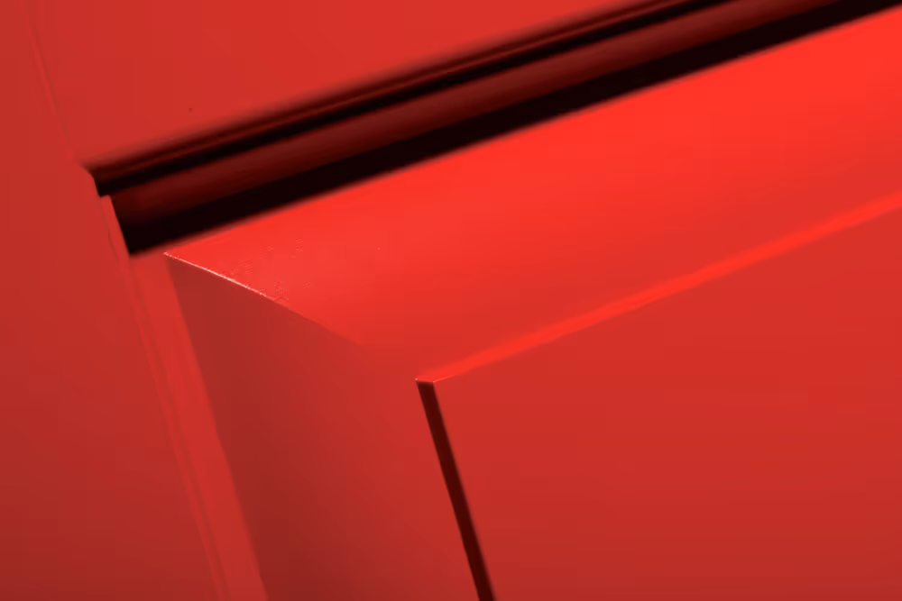 Close-up of a red door corner showing smooth surface and black door seal on top edge.