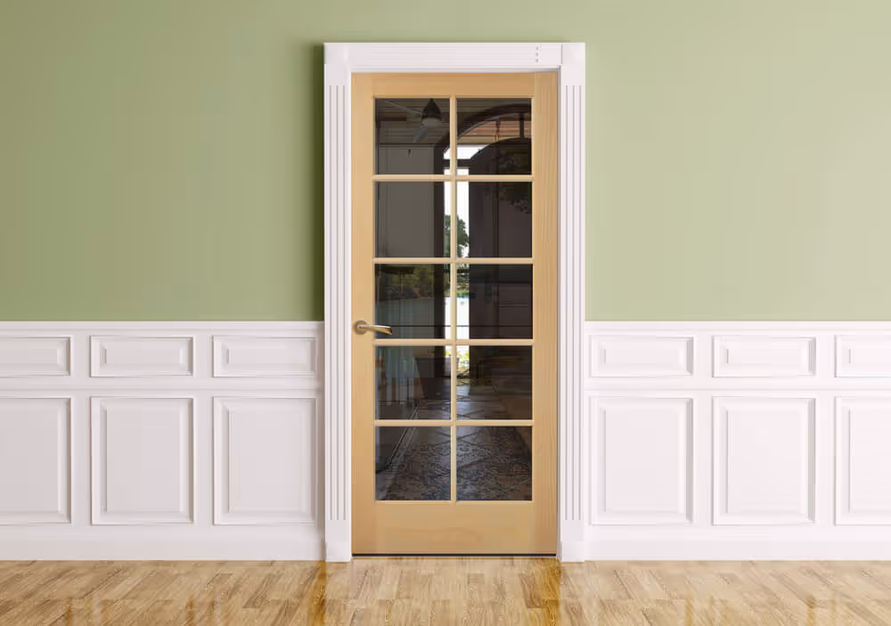 Light wood interior door with nine glass panes, framed by white molding, set in a green and white paneled wall above a hardwood floor.
