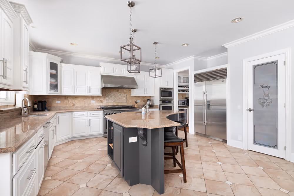 Spacious modern kitchen with white cabinets, beige countertops, center island with seating, stainless steel appliances, and a pantry door.
