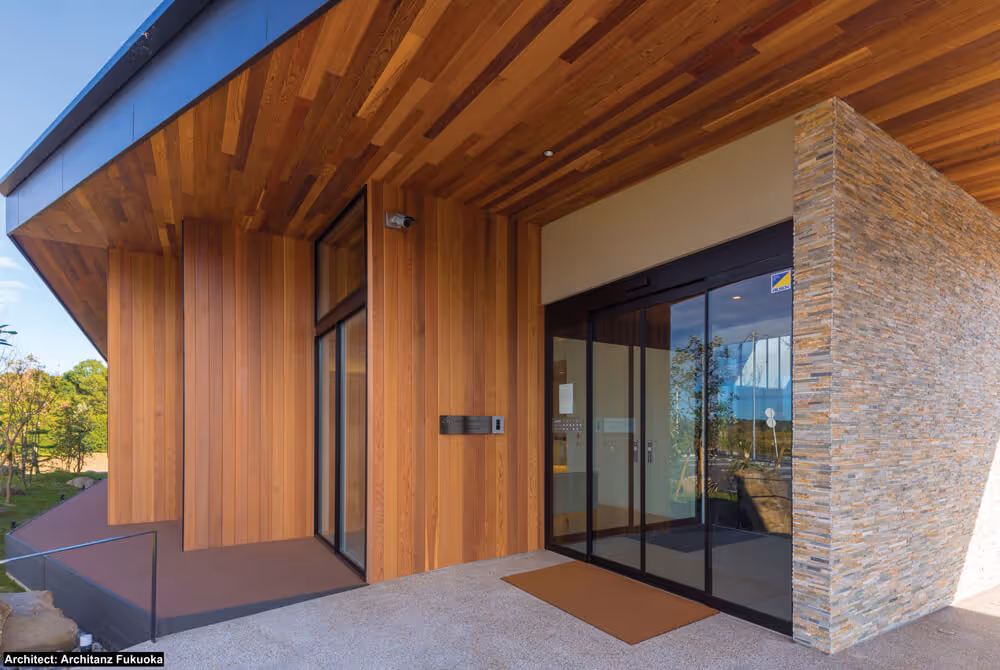 Modern building entrance with vertical cedar wood siding, stone wall, glass sliding doors, and a brown doormat.