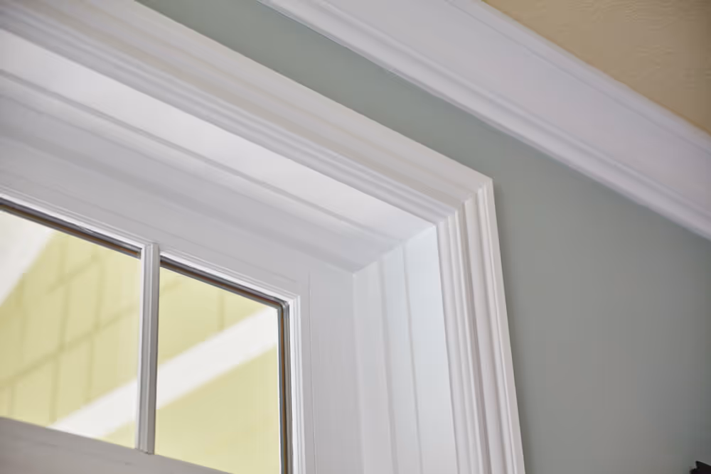 Close-up of white decorative window casing and light green wall with white crown molding.