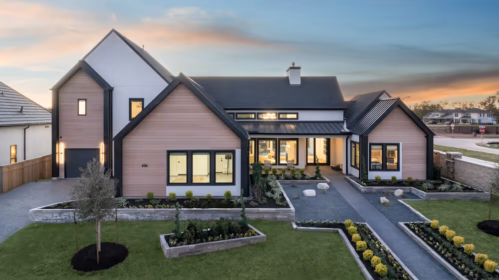 Modern single-story house with large windows, pink siding, black roof, and landscaped yard at sunset.