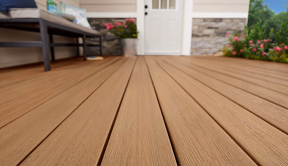 Close-up of smooth brown wooden deck boards on a patio with outdoor bench, flower pot, and house door in the background.