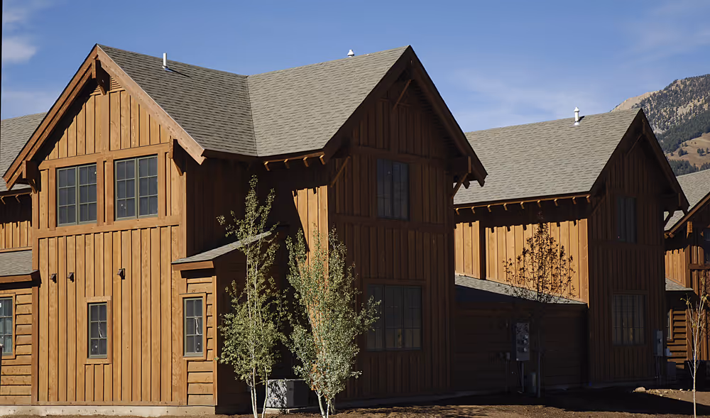Wooden houses with steep gray roofs and small trees in front under a blue sky.