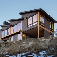Modern cabin with large windows elevated on stilts on a rocky hillside.