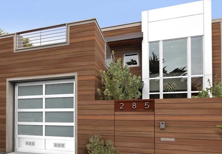 Modern house exterior with horizontal wooden cladding, a large white-framed window, and a garage door, showing house number 285 on the wooden fence.