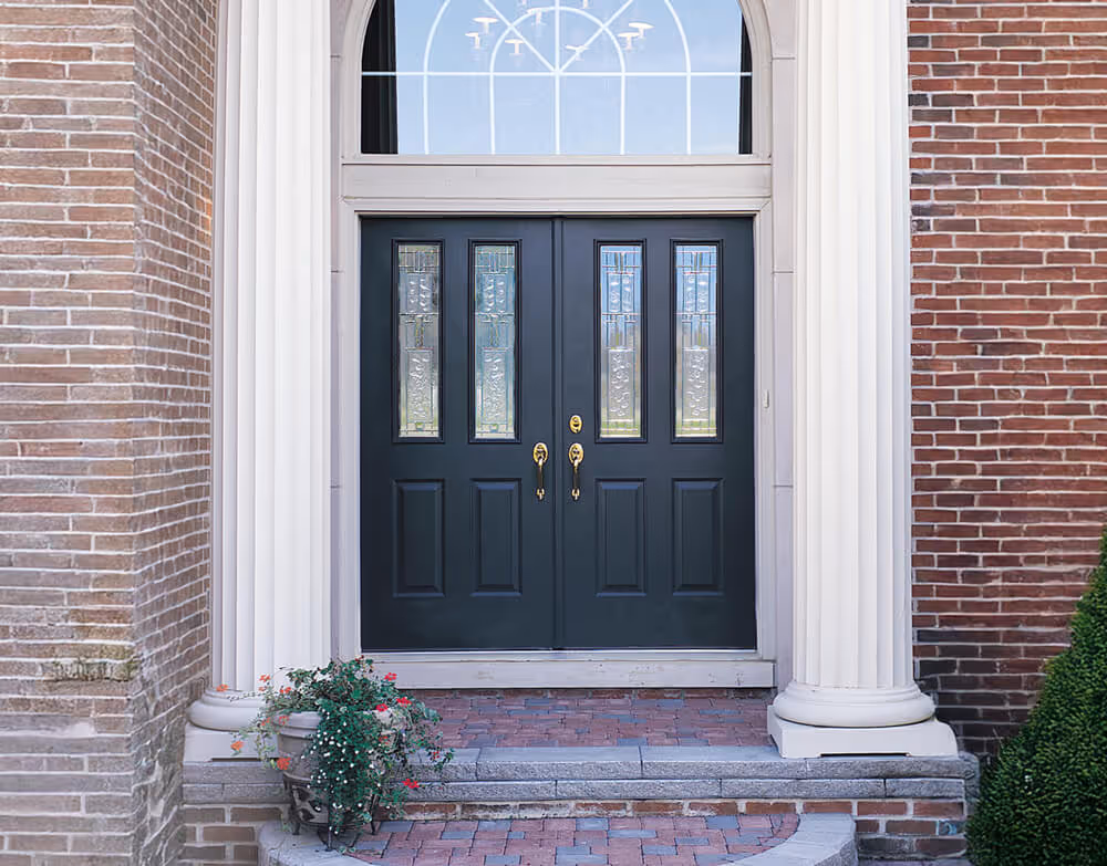 Black steel double doors with decorative glass panels and brass handles, framed by white columns and red brick exterior.