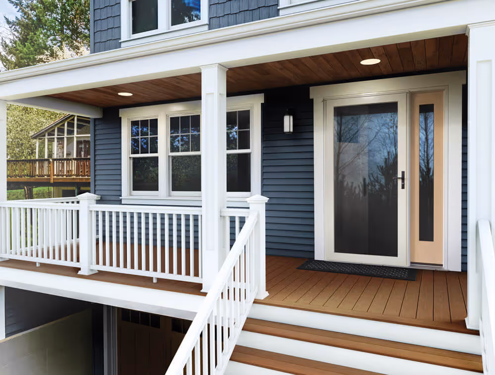 Front porch with white railing, brown wood decking, blue siding, and glass-panel front door with sidelights.