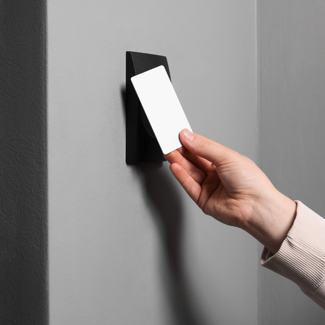Hand holding a white key card next to a black card reader on a gray wall.