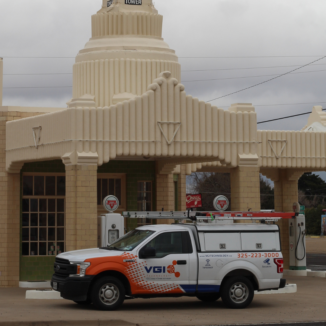 White and orange VGI Technology service truck parked at a vintage Conoco gas station with a beige art deco canopy.