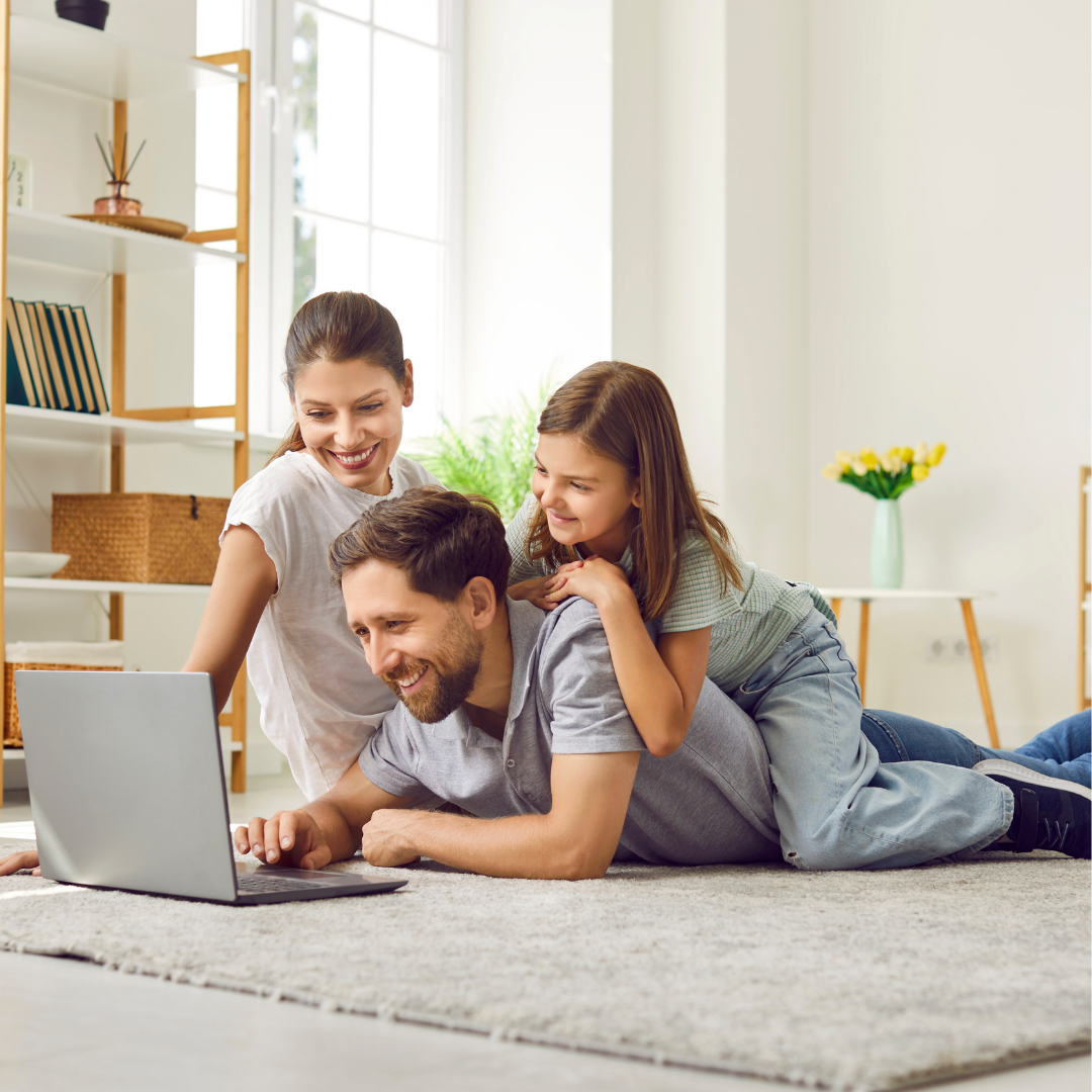 Smiling family of three lying on floor looking at laptop in bright room.