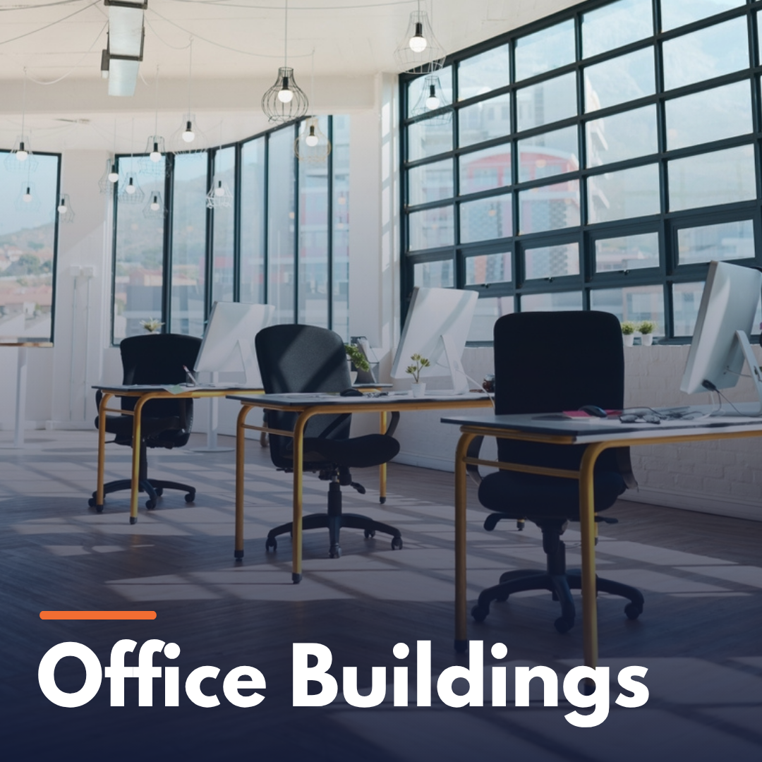 Modern office interior with large windows, several desks, chairs, and computer monitors.