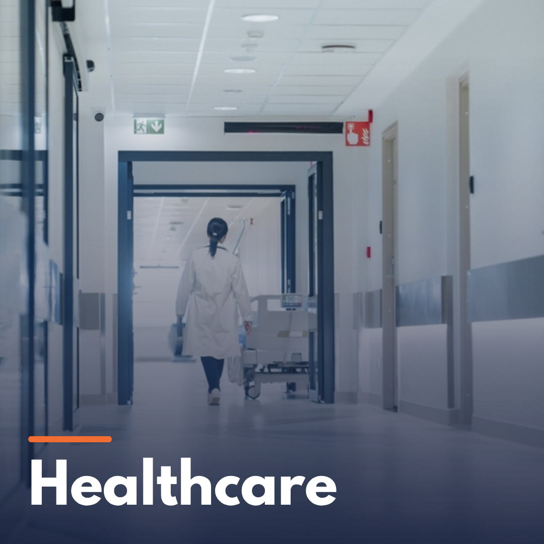 A healthcare professional walking down a hospital corridor with a bed and medical equipment.