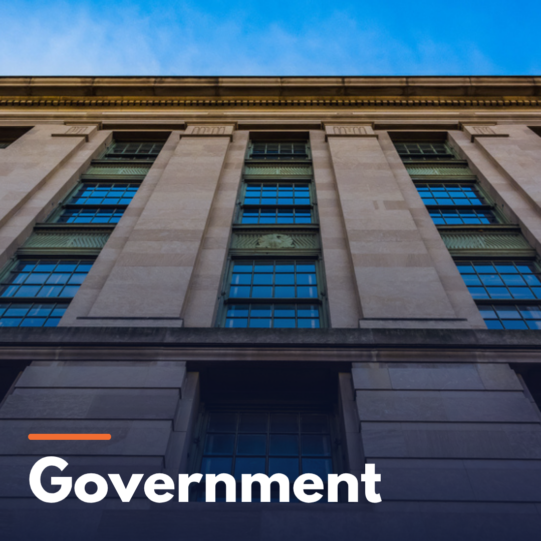 Low-angle view of a government building with tall windows and stone facade against a blue sky.
