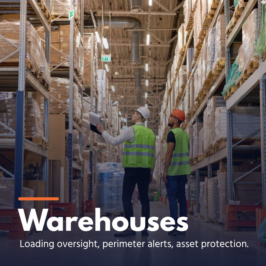 Two warehouse workers with helmets and vests inspecting tall shelves loaded with wrapped pallets.