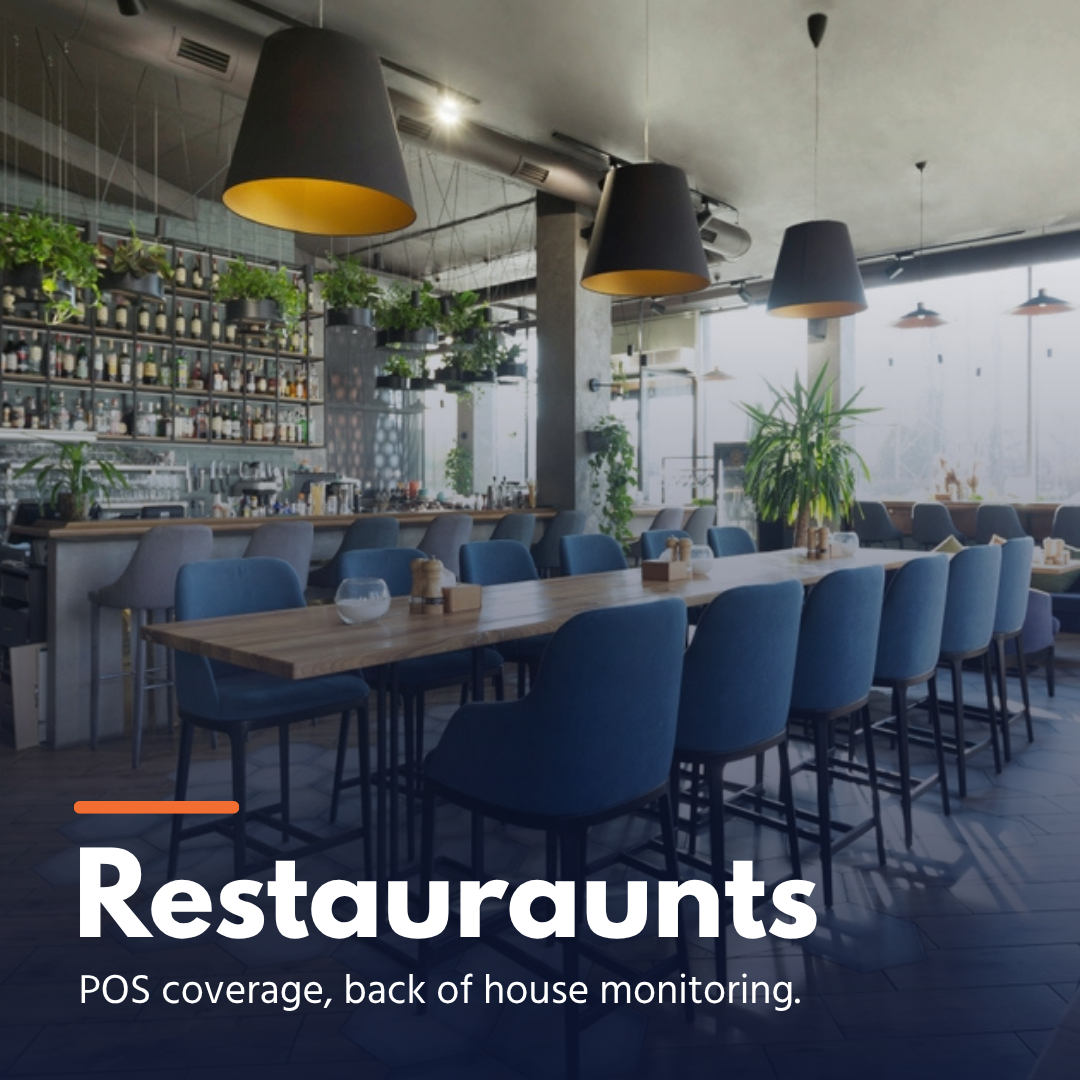 Modern restaurant interior with long wooden table, blue chairs, hanging lamps, and plants.