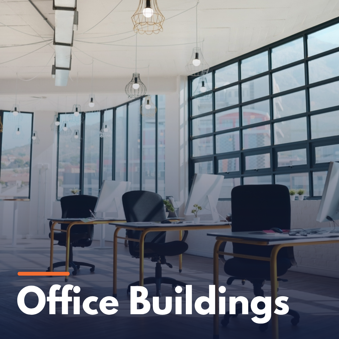 Modern office interior with desks, black chairs, computers, and large windows showing city buildings.