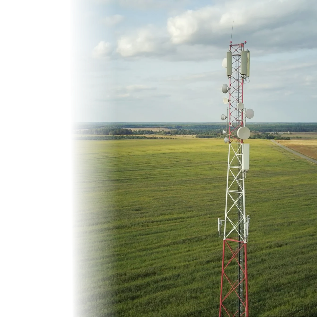 Tall red and white communication tower with multiple antennas standing in a green field under a cloudy sky.