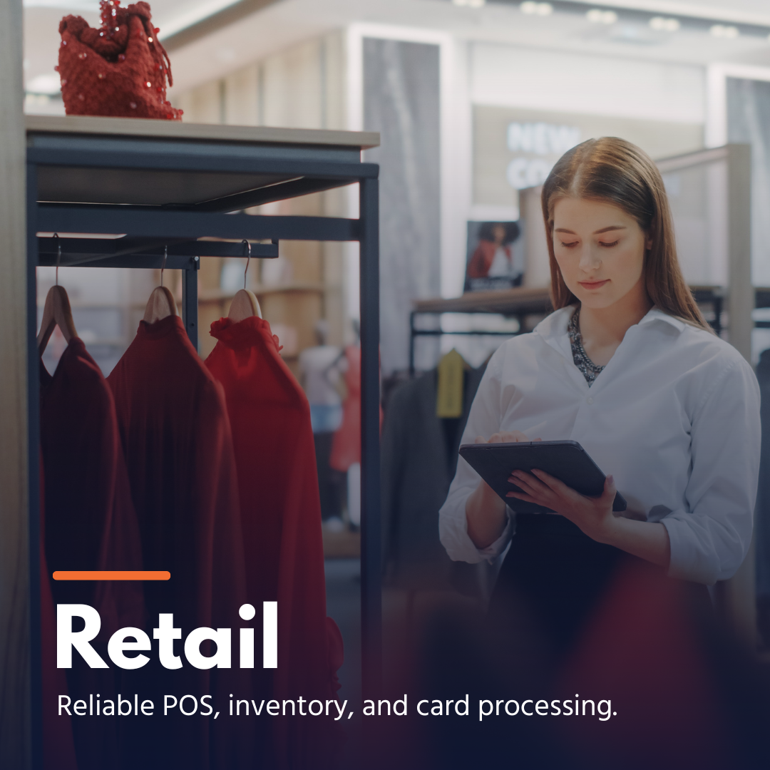 Woman in white shirt using tablet near clothing rack with red dresses in a retail store.