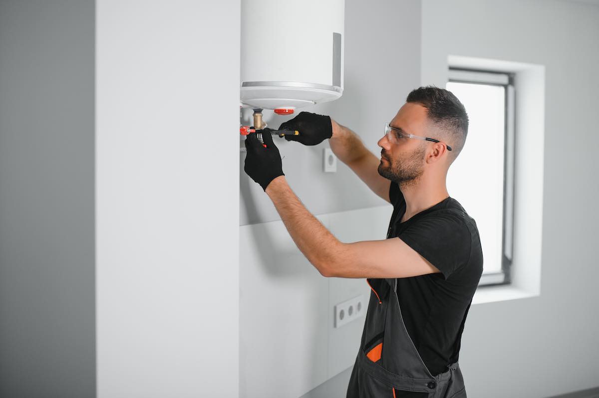 Technician in black gloves installing white boiler on wall indoors