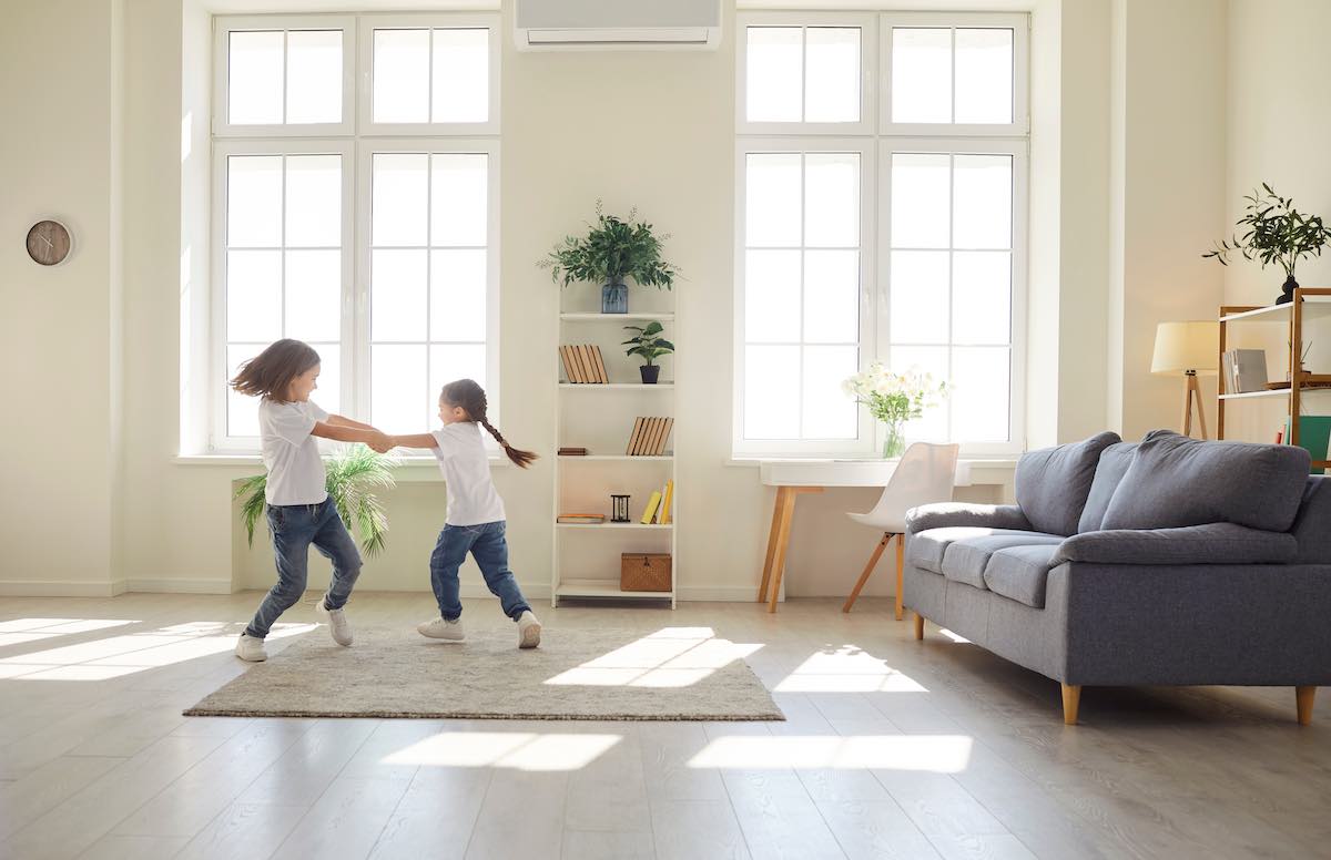 Two children playing and dancing in bright, modern living room with large windows