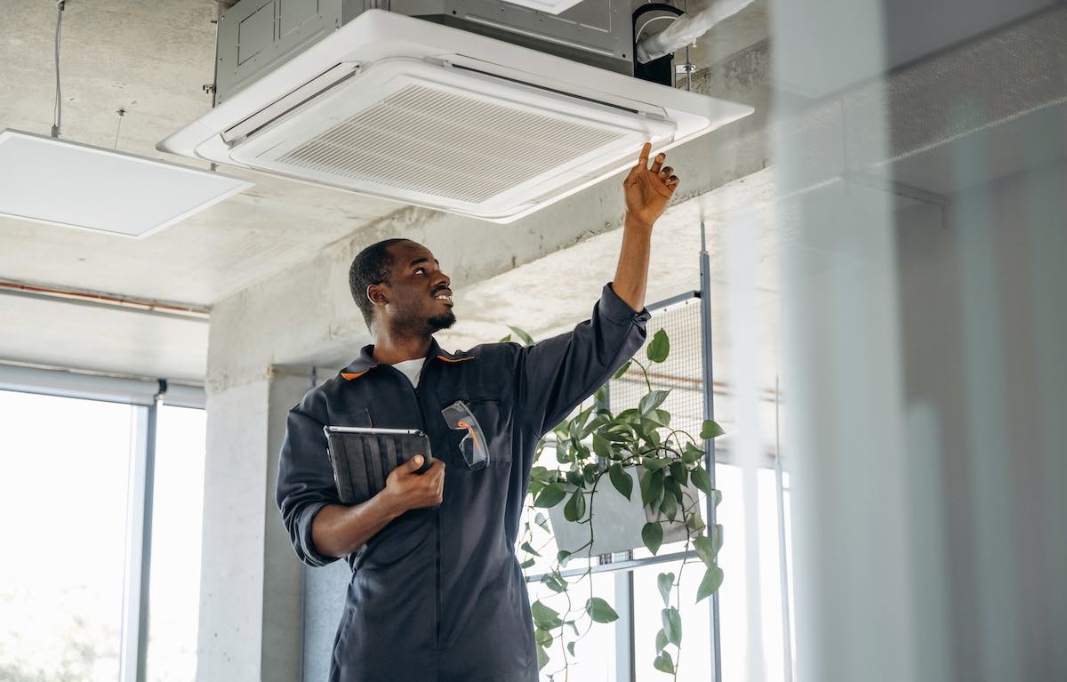 HVAC technician inspecting ceiling-mounted air conditioning unit indoors