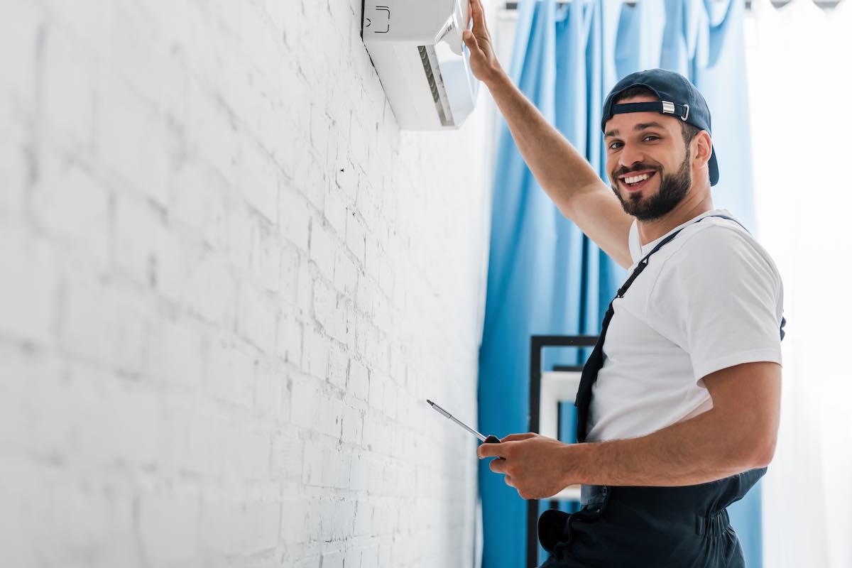 Electrician installing switch on white brick wall, smiling at camera