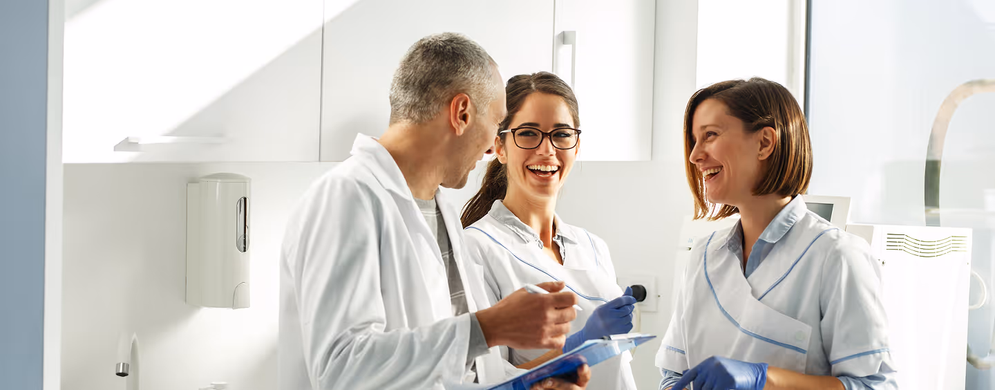 Three healthcare professionals smiling and conversing in a bright medical office.