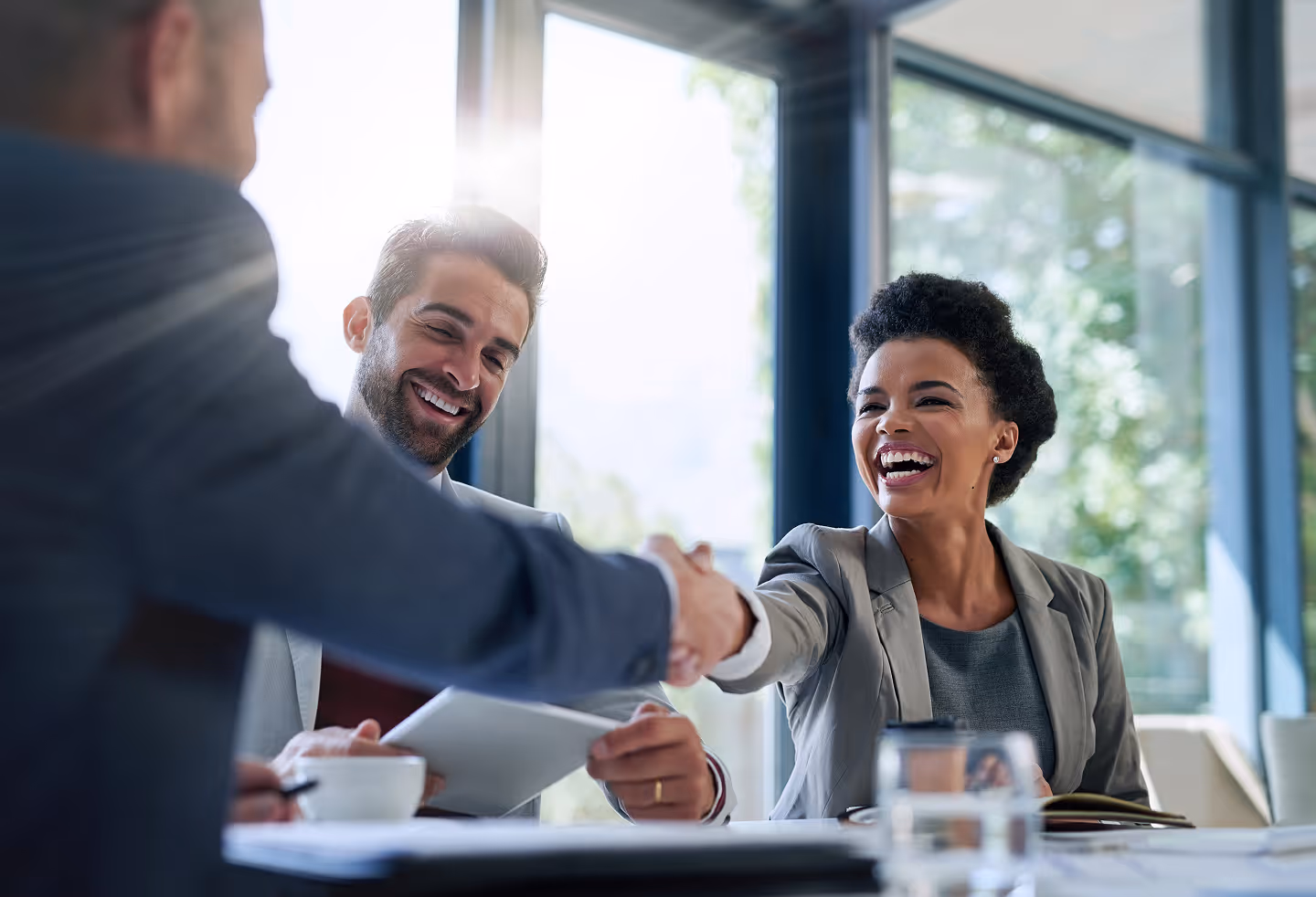 Smiling businesswoman and businessman shaking hands across a table in a bright office.