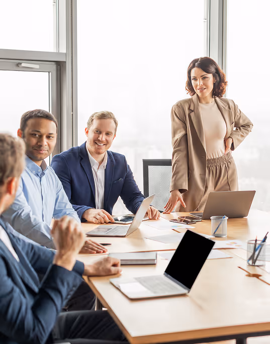 Four business professionals having a meeting around a table with laptops and documents in a bright office.