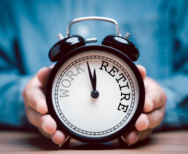 Hands holding a black alarm clock with words work and retire on its face, time near 12 o'clock.
