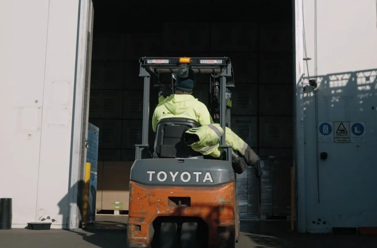 Person operating a Toyota forklift entering a warehouse with safety gear on.