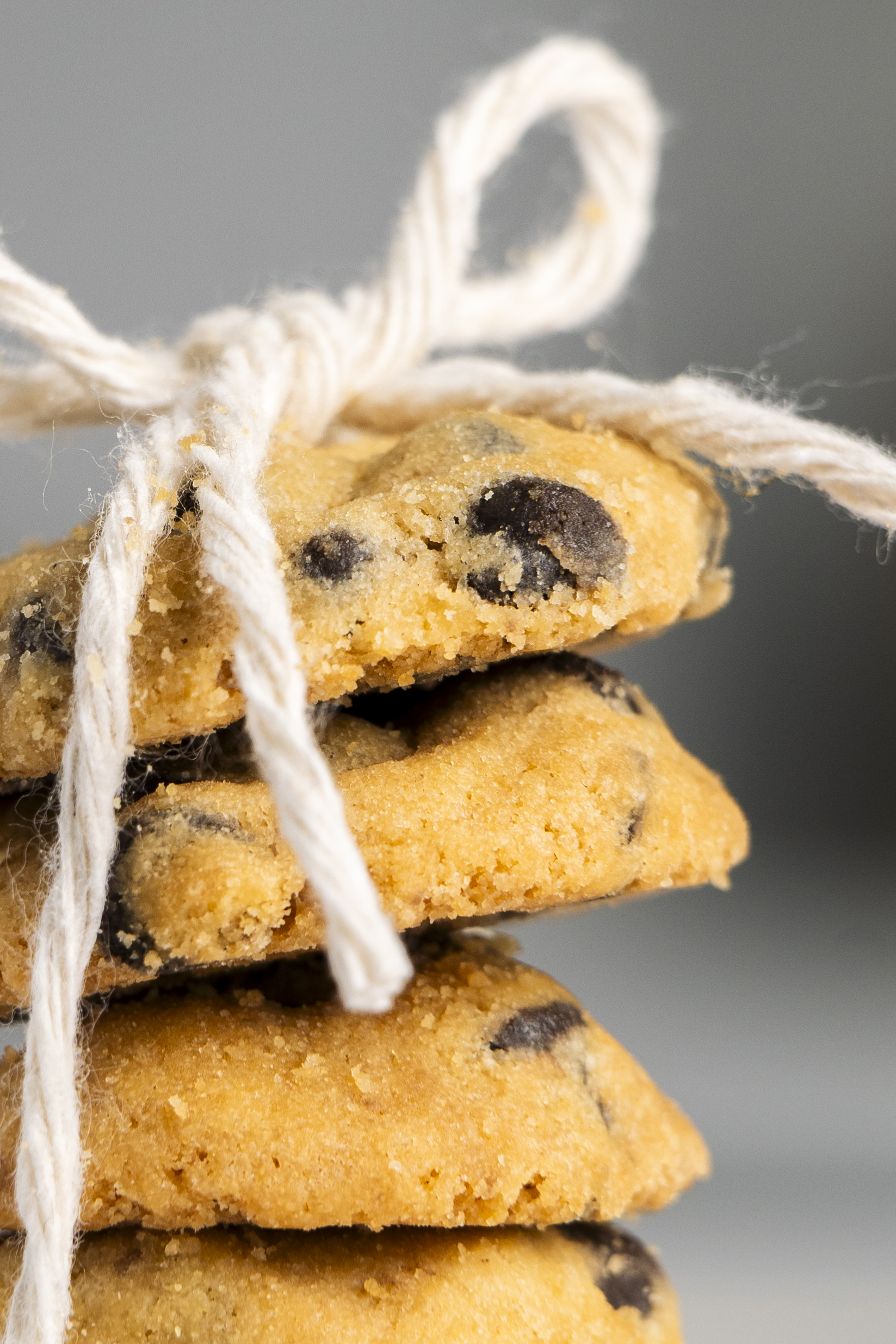 Stack of chocolate chip cookies tied with a white string bow on a gray background.