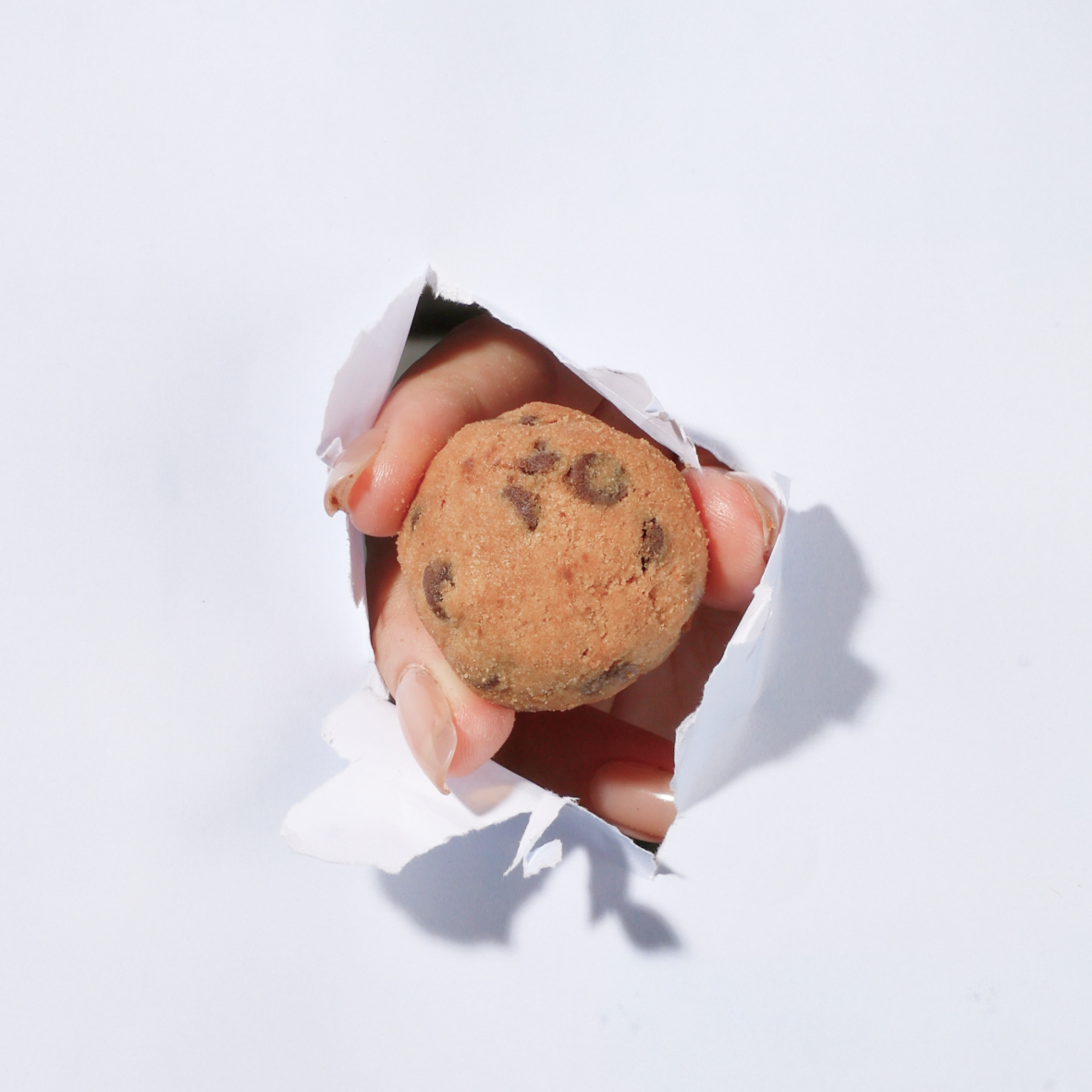 Hand picking a chocolate chip cookie from a metal bowl filled with cookies on a rustic cloth surface.