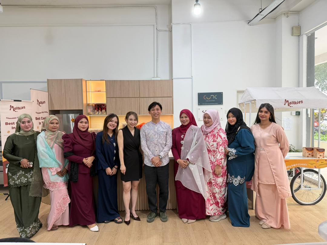 Group of ten people standing indoors, dressed in colorful traditional and modern outfits, posing for a photo in front of a wooden cabinet and a cart with Meltkies branding.
