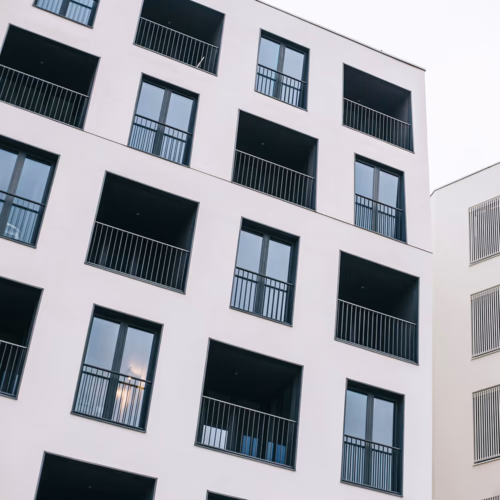 Modern apartment building facade with black-framed windows and balconies against a light sky.