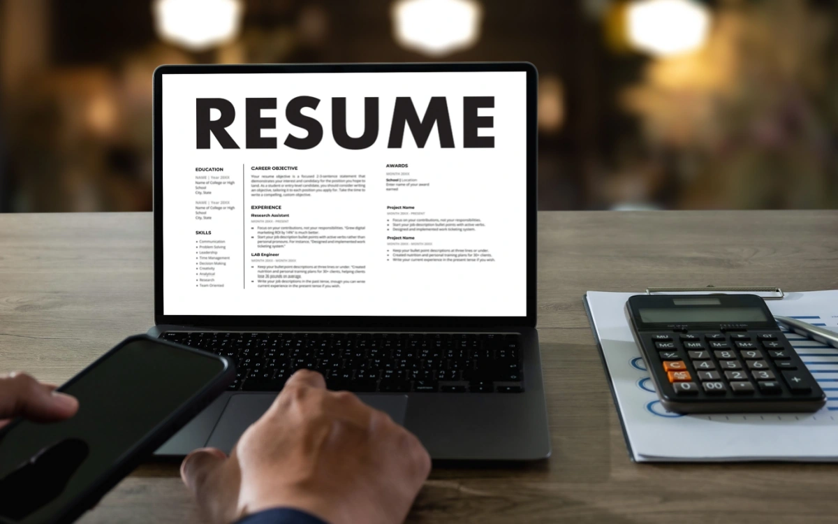 Employer reviewing a resume on a laptop with phone and documents, representing AI-generated resumes and the need for background checks to verify candidate claims and reduce hiring risk.