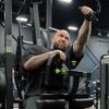 Bearded man using a cable machine for a shoulder workout in a gym.