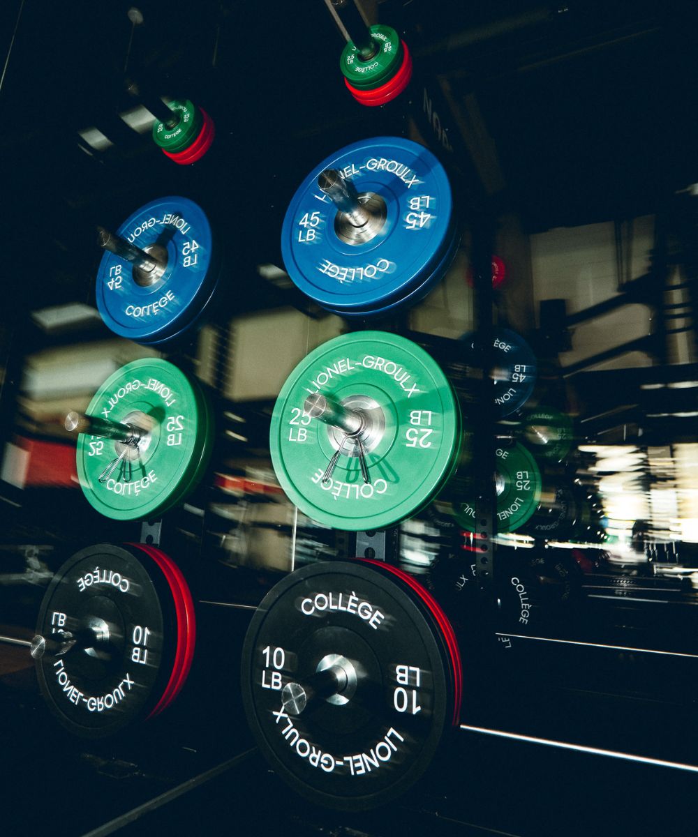 Stacked colorful weight plates on a gym rack reflected in a mirror.