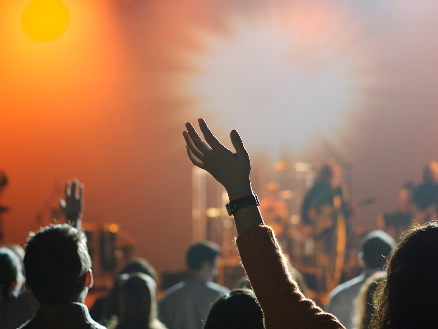 Crowd at a concert raising hands towards the stage with bright lights in the background.