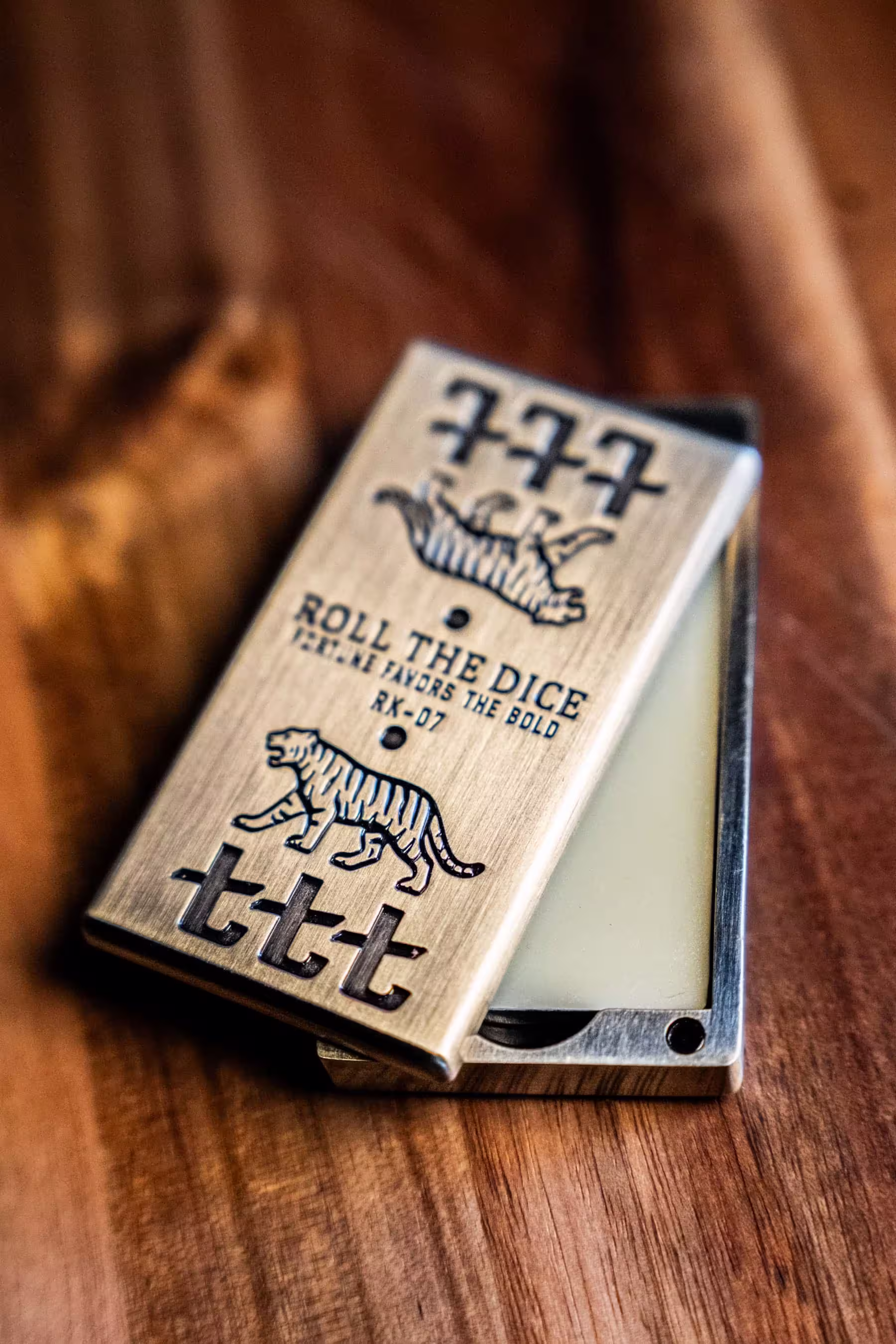 Metal game case with tiger graphic, crown, and text 'Roll the Dice Fortune Favors the Bold' on wooden surface.