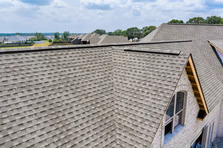 Aerial view of newly installed gray architectural shingles covering large hip roof with multiple valleys and dormers.