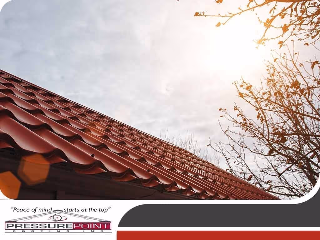 Red metal roofing with textured tiles under a cloudy sky, featuring the Pressure Point Roofing logo and the phrase "Peace of mind starts at the top," emphasizing residential roofing services.