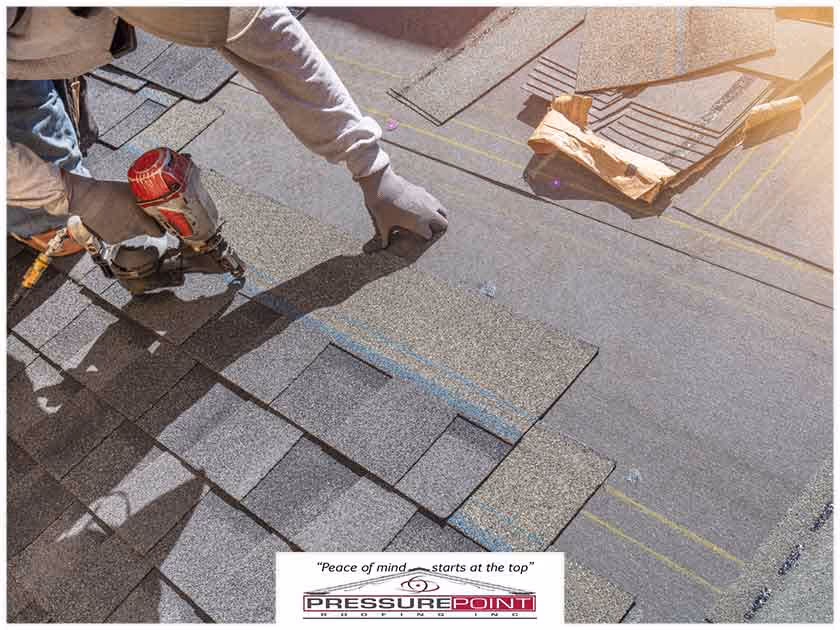 Worker installing shingles on a roof with a nail gun, showcasing roofing techniques and materials, branded with Pressure Point Roofing logo and slogan.