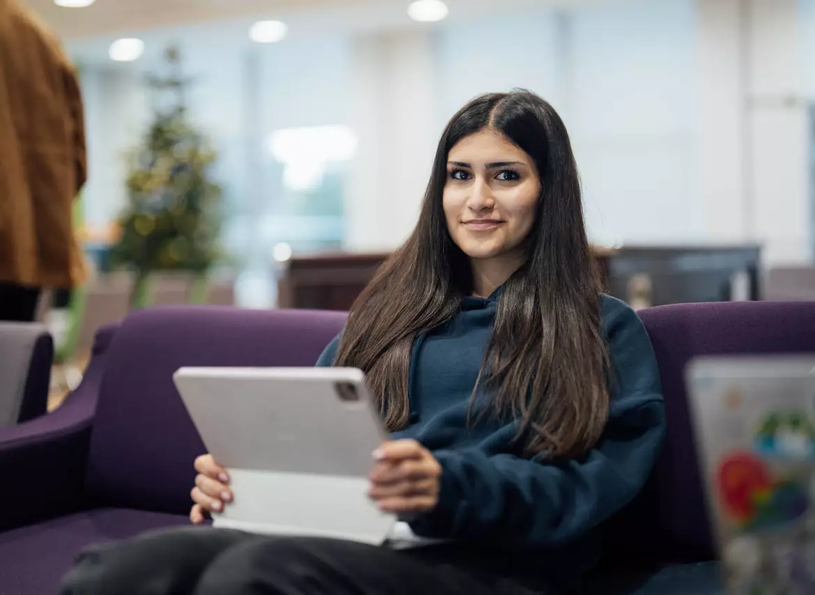 A girl with long, dark hair is holding a laptop.
